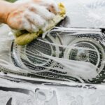 Hand scrubbing a car headlight with sponge and soap suds, detailing process.
